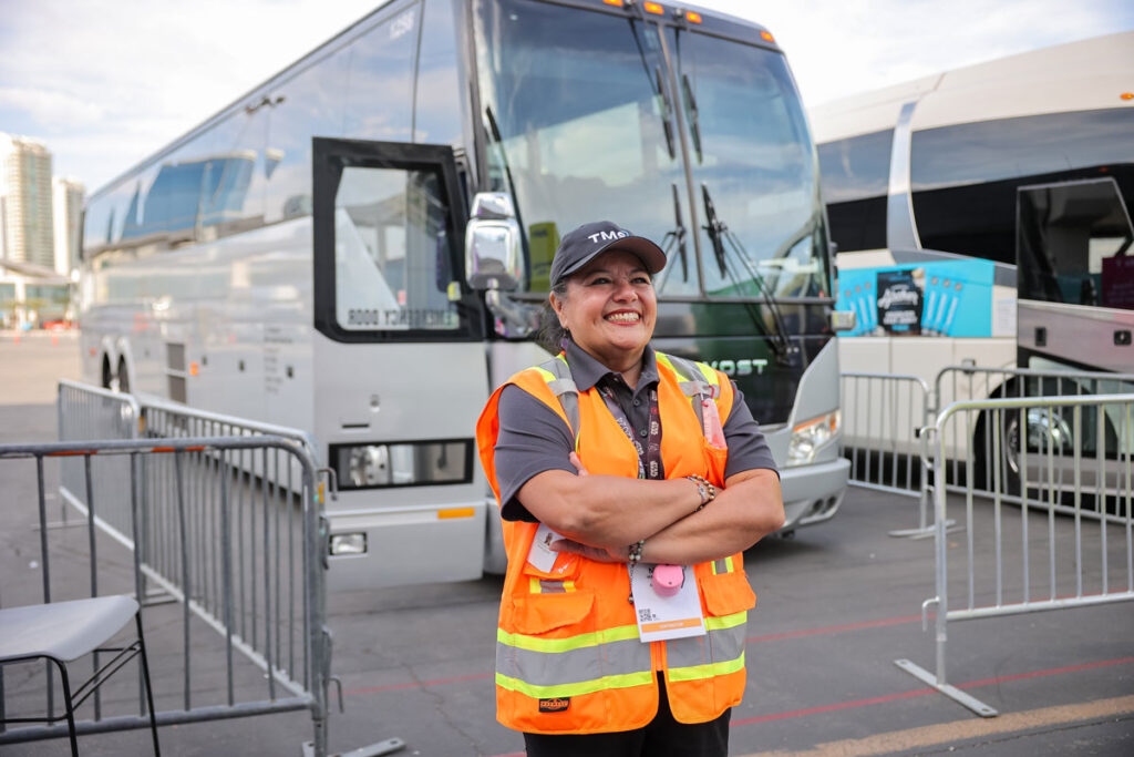 smiling TMS worker with orange vest and smiling with shuttle bus in the background