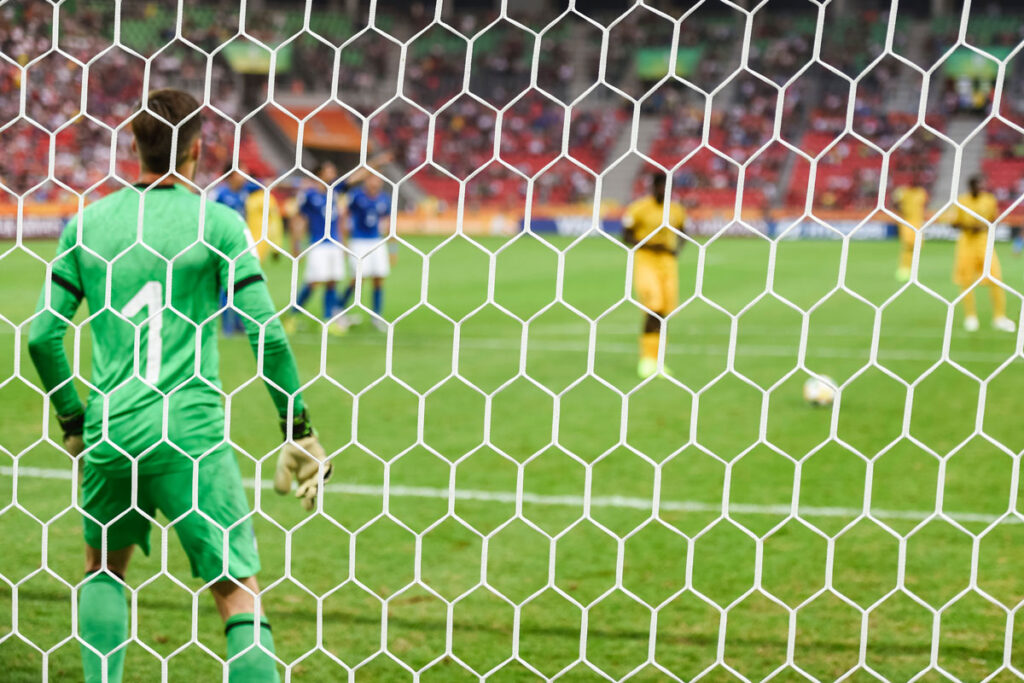 picture taken through a soccer goal of a goalie and players on the field